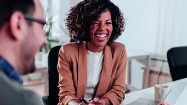 Três pessoas conversando e rindo em uma reunião de trabalho.