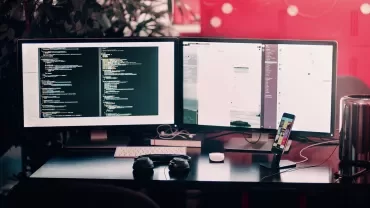 Estação de trabalho com dois monitores exibindo código de programação.
