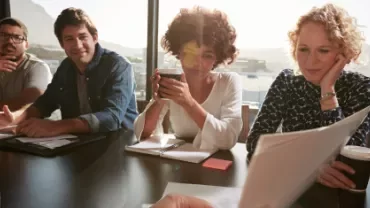 Grupo de pessoas em reunião ao ar livre, olhando para documentos.