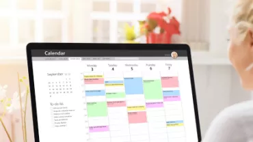 Mulher branca loira com o cabelo preso trabalhando no computador organizando um calendário