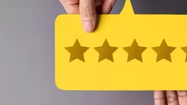 Cartão amarelo com cinco estrelas marrons entre dedos.