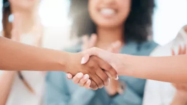 Grupo comemorando enquanto duas pessoas apertam as mãos