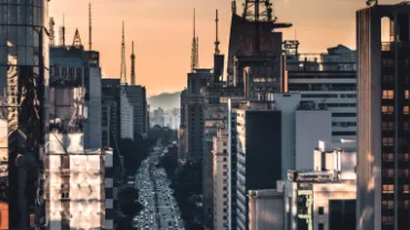 Imagem que ilustra a cidade vista de cima, com vários prédios sendo iluminados pelo pôr do sol.