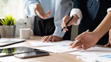Pessoas trabalhando juntas em gráficos e relatórios de reunião sobre uma mesa.