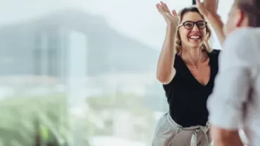 Mulher sorridente faz high-five com colega em escritório.