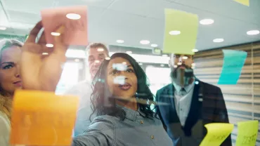 Equipe colaborando em frente a um quadro de notas adesivas coloridas.