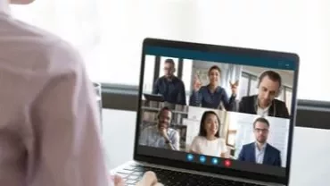 Pessoa participa de uma videoconferência com várias pessoas na tela do laptop.