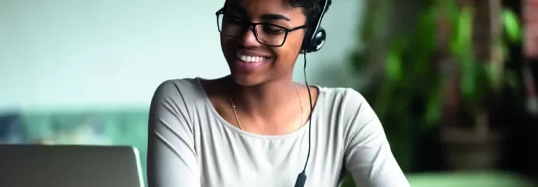 Mulher sorrindo, usando fones de ouvido e olhando para laptop.