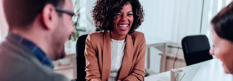 Três pessoas conversando e rindo em uma reunião de trabalho.