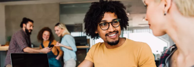 Homem negro de cabelo cacheado sorrindo para a colega de trabalho