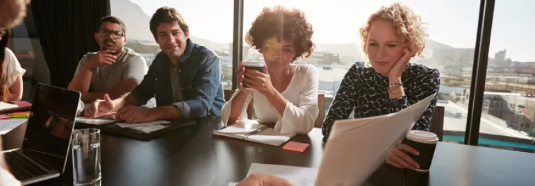 Grupo de pessoas de diversas etnias conversando sobre trabalho sentados em uma mesa