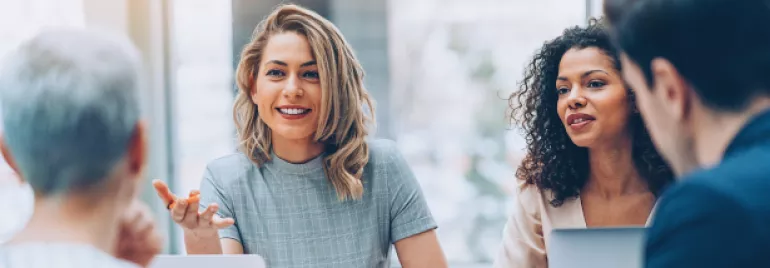 Mulheres de diferentes idades e etnias sentadas ao redor de uma mesa, trabalhando e conversando