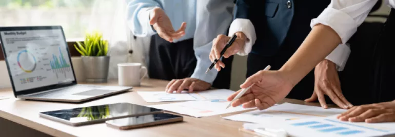 Pessoas trabalhando juntas em gráficos e relatórios de reunião sobre uma mesa.