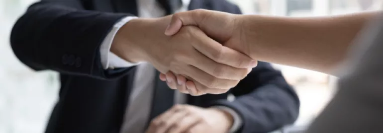Imagem focada em um aperto de mãos entre duas pessoas, simulando um ambiente de contratação.