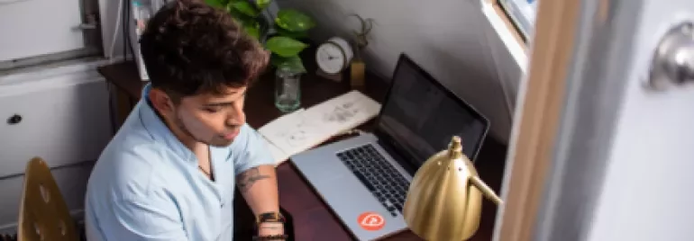 Pessoa escrevendo em caderno ao lado de laptop em mesa de trabalho.