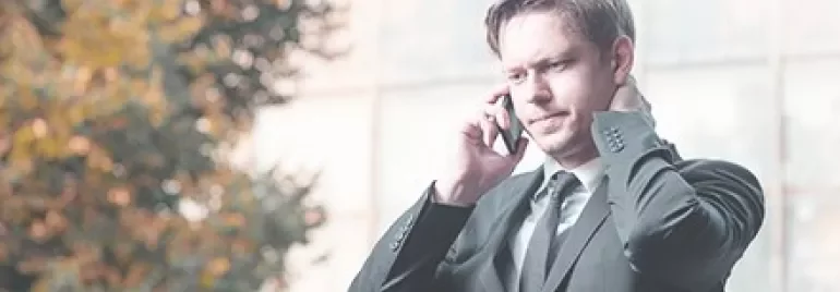 Homem em terno escuro falando ao celular ao ar livre.