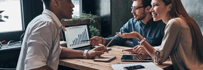 Três pessoas discutindo gráficos em uma reunião de trabalho.