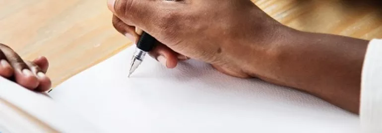 Pessoa escrevendo em um caderno com caneta preta.