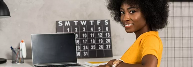 mulher negra sorrindo sentada em frente a um computador