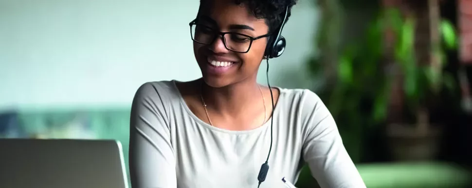 Mulher sorrindo, usando fones de ouvido e olhando para laptop.