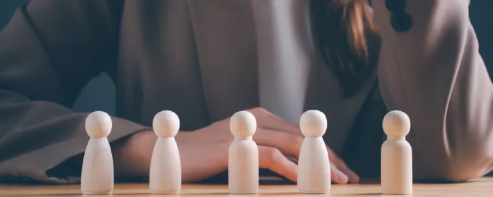 Mulher observando cinco figuras de madeira sobre a mesa.