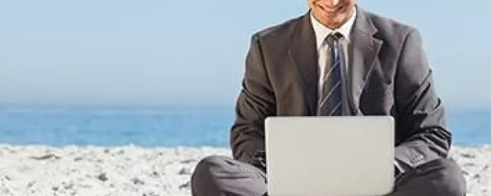 Homem de terno usando laptop na praia.