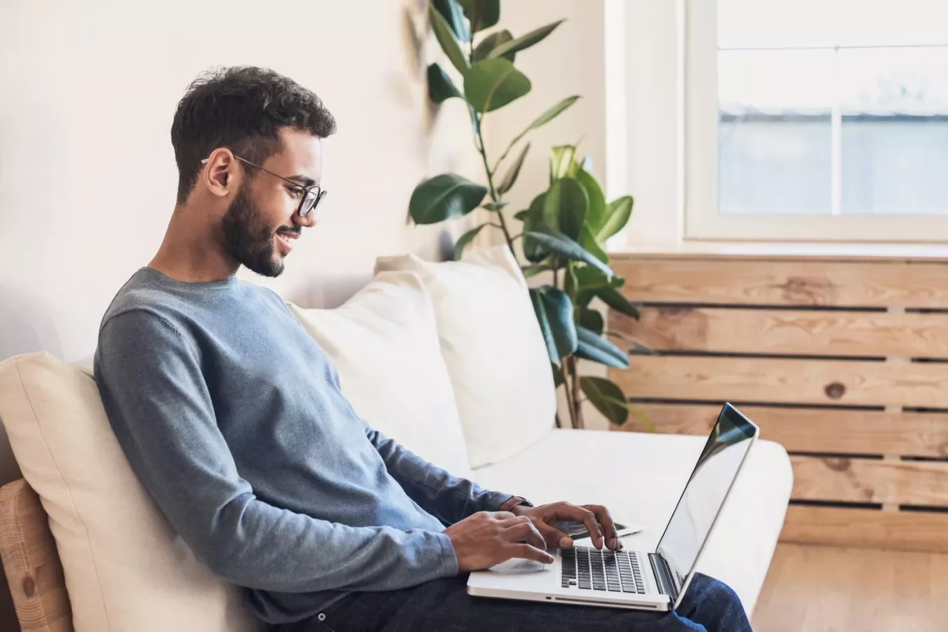 Homem sorridente usa laptop enquanto está sentado em um sofá confortável.