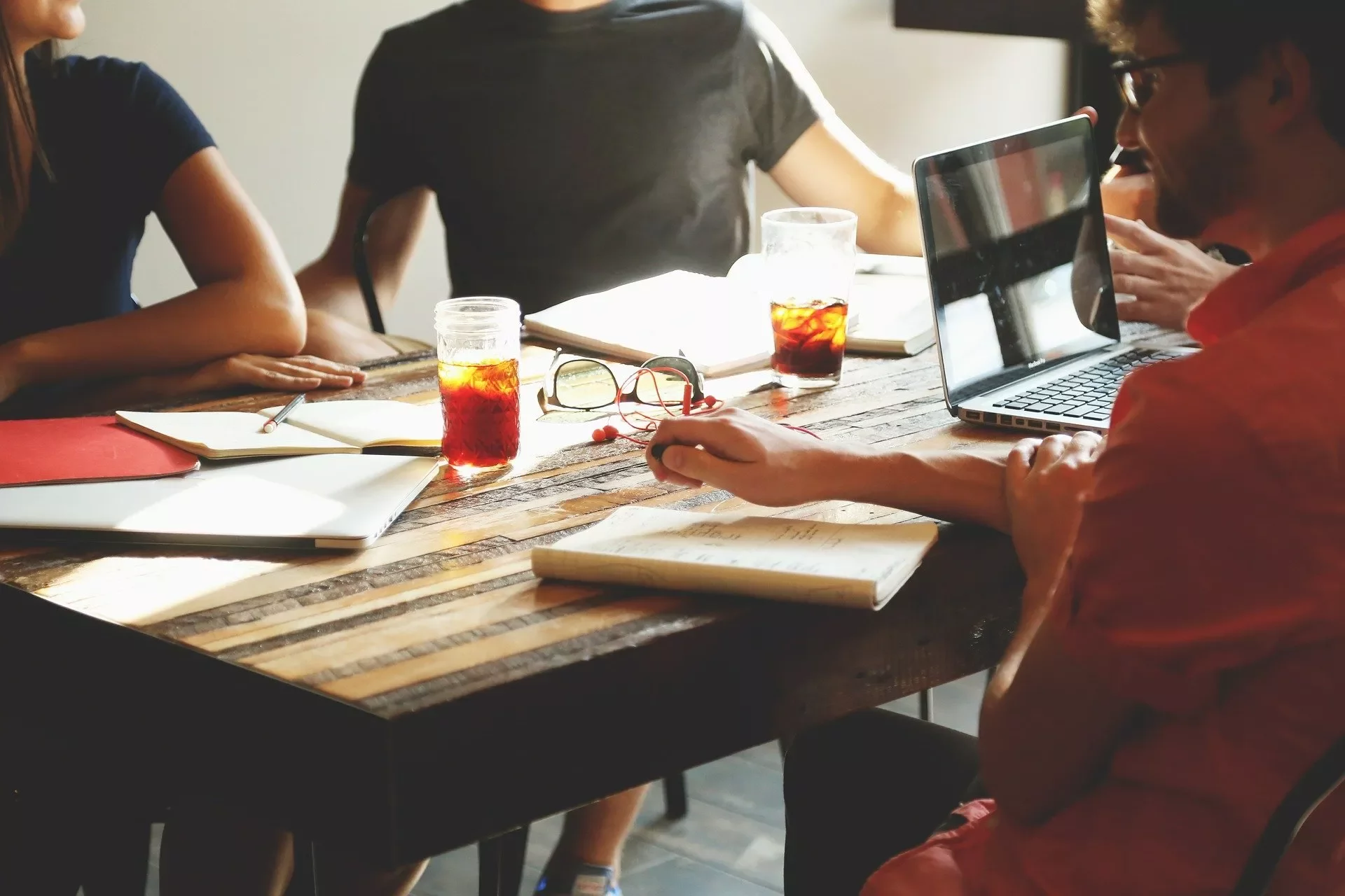 Grupo reunido em mesa de madeira com laptops e bebidas.