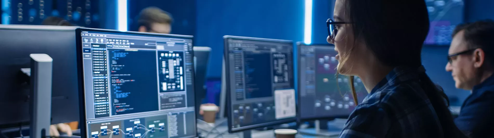 Pessoas trabalhando em computadores com código em uma sala de TI.