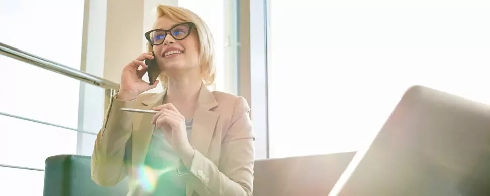 Mulher sorridente falando ao telefone em um escritório iluminado.