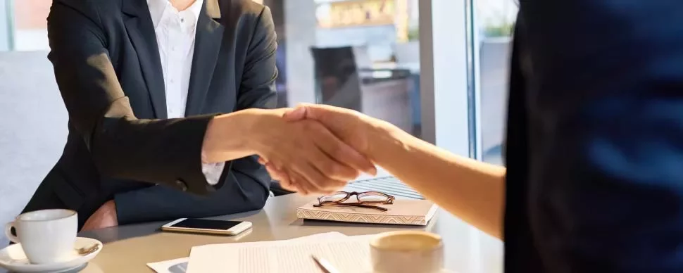 Duas pessoas apertando as mãos em uma mesa de reunião.