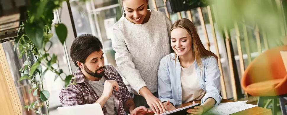 Três pessoas sorrindo trabalham juntas em um tablet.