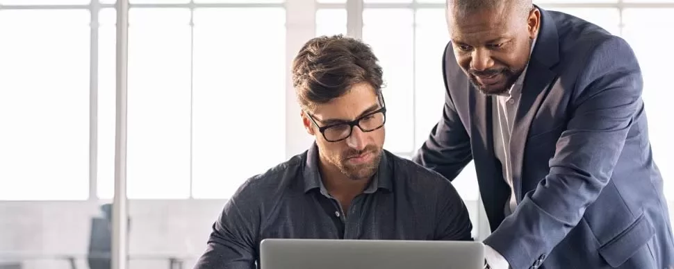 Dois homens trabalhando juntos em frente a um laptop.