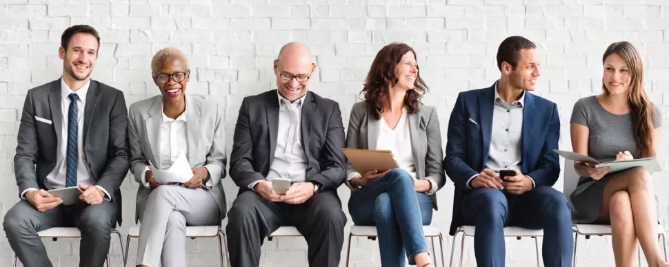 Grupo de pessoas sentadas em fila, vestidas formalmente e sorrindo.