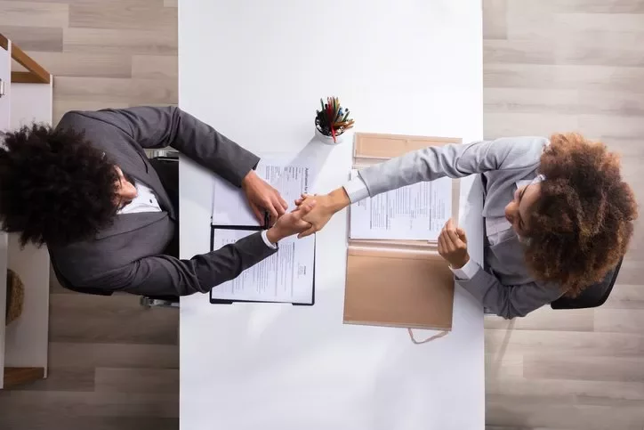 Duas pessoas apertando as mãos sobre uma mesa com documentos.