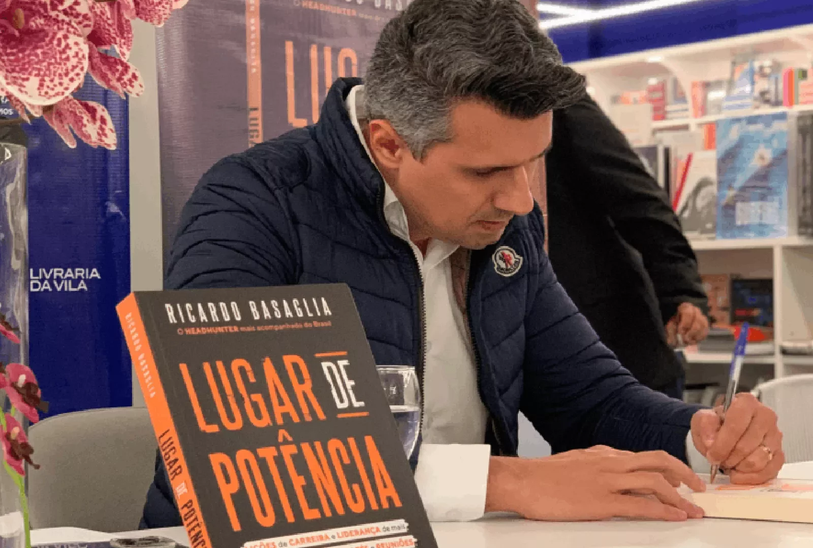 Autor autografando livro em livraria com livro 'Lugar de Potência' na mesa.