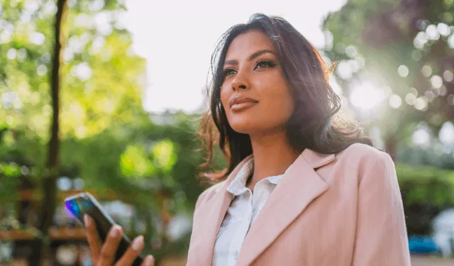 Mulher ao ar livre segurando um smartphone, olhando pensativa.