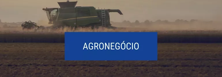 Colheitadeira trabalhando em campo de trigo ao entardecer, com destaque 'Agronegócio'.