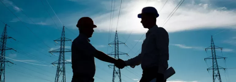 Engenheiros cumprimentam-se em frente a linhas de alta tensão.