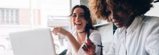 Duas mulheres jovens animadas trabalhando juntas em um laptop.