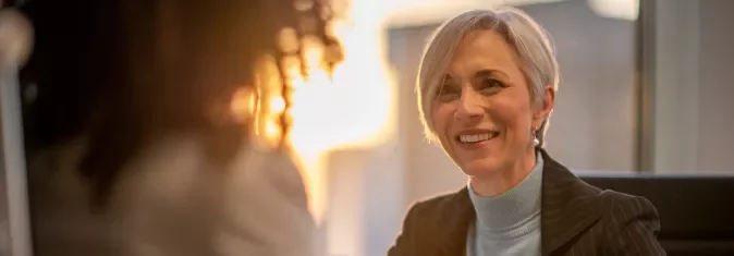 Mulher sorrindo durante uma reunião em um escritório iluminado pelo sol.