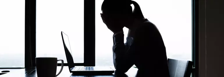 Pessoa olhando para laptop, mãos no rosto, em escritório iluminado.