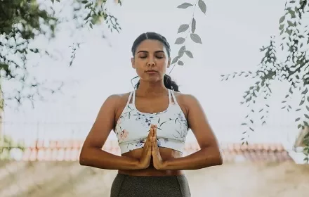 Mulher jovem praticando ioga ao ar livre com olhos fechados.