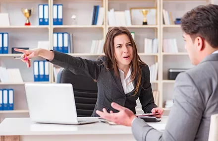 Mulher apontando e discutindo com homem em escritório.