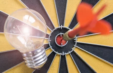 Lâmpada e dardo em alvo, simbolizando ideias e metas.