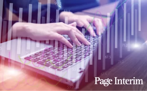 Pessoa digitando em teclado de computador com gráficos ao fundo.