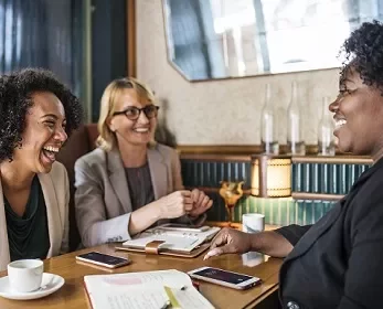 Três mulheres conversando e sorrindo em um café.