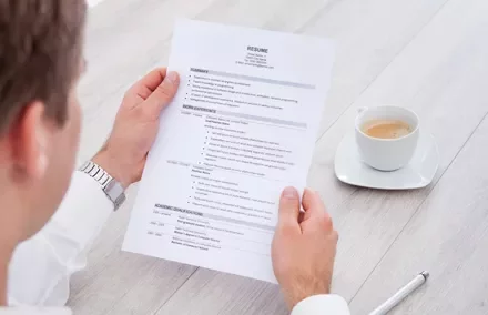 Pessoa segurando um currículo com uma xícara de café na mesa.