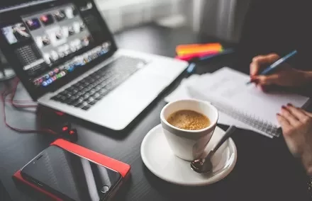 Café em mesa de escritório com laptop e caderno.