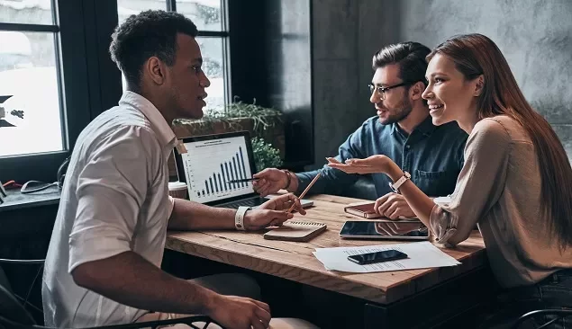 Três pessoas discutindo gráficos em uma reunião de trabalho.